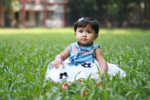A little girl in a dress sits on the grass.