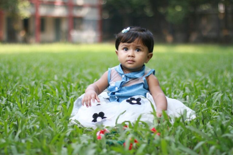 A little girl in a dress sits on the grass.